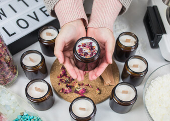 Hands hold a handmade ecological and vegan soy wax candles with dried flowers. Amber and opaque container. Cruelty-free vegan product.