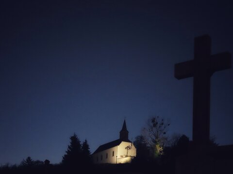 White illuminated Christian church and silhouette of a cross at dark night 