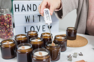 Measuring the temperature of handmade ecological and vegan soy wax candles. Amber and opaque container. Candle making utensils. Cruelty-free vegan product, handmade with love