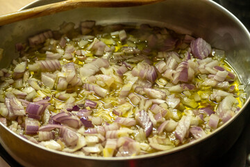 Clos up of chopped onions getting fried in a pan with oil.