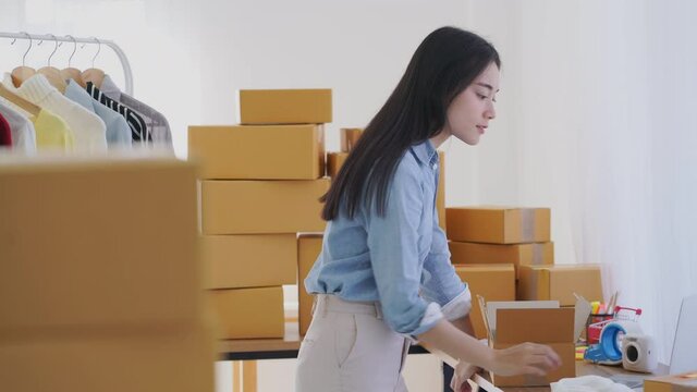 Asian business entrepreneur woman packing dress clothes in mailing box for shipping from online store