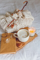 Home cozy decor. A mug of cappuccino, cookies, a candle on the bed. Winter morning.