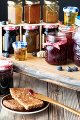 Close up of a variety of different types of jam in jars and honey with toast in front.