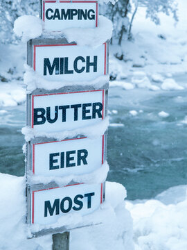 signpost for selling dairy products covered with ice and snow, written in german language