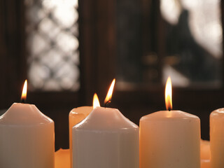 pile of burning white candles with a church window in the background
