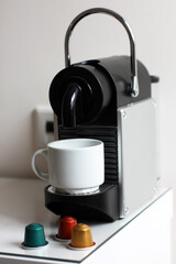 Coffee machine with white cup and coffee capsules against the background of a white wall horizontally. 