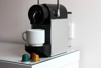 Coffee machine with white cup and coffee capsules against the background of a white wall vertically. 