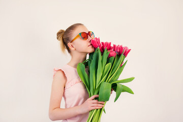 teenage girl in fancy pink glasses holding a huge bouquet of fresh tulips on white background