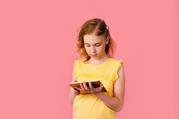 A teenage girl does her homework on a tablet. The student works and communicates with friends. Pink background with free space