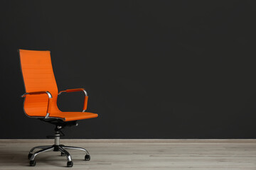 Comfortable office chair near black wall indoors. Space for text