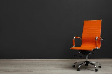 Comfortable office chair near black wall indoors. Space for text