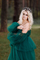 young beautiful blonde hair woman queen. Princess walks. autumn green forest mystic. Vintage medieval shiny crown. Long evening green dress. magic fantasy