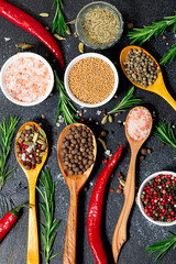 Assortment of spices and herbs in the wooden spoons on black rustic background top view. Cook book cover template. Vertical spices banner.