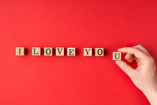 I love you concept. Above close up flat lay view photo of female hand writing phrase using wooden blocks isolated bright color backdrop