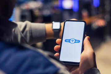 Man holds a smartphone with a close-up wi-fi icon and a smart watch on his hand.