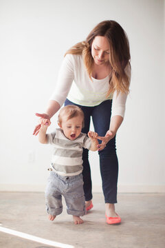 Young mother assisting baby boy (6-11 months) in first steps