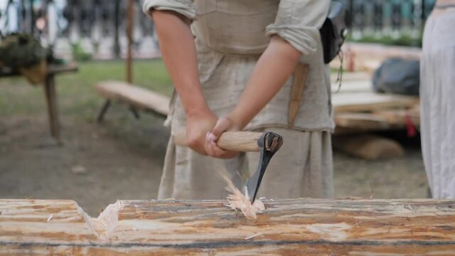 Man lumberjack cutting large log with axe - wood shavings, chips flying at summer historical medival festival - close up, slow motion. Craftsmanship, revival, reenactment, handwork concept