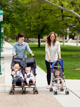 USA, Utah, Salt Lake City, Two young mothers walking with two baby boys (6-11 months) and toddler girl (2-3) in push prams