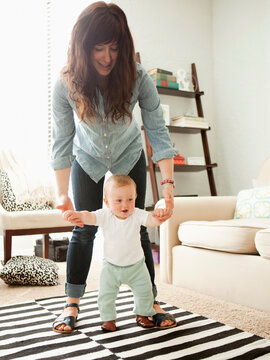 Young mother assisting baby boy (6-11 months) in his first steps