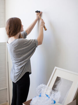 Young woman hanging picture on freshly painted wall