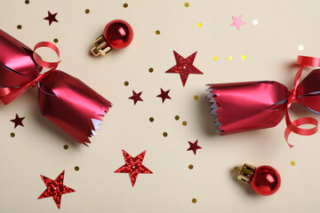 Open red Christmas cracker and decorations with shiny confetti on beige background, flat lay