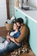 young couple in stylish casual clothes embracing with closed eyes on floor in kitchen