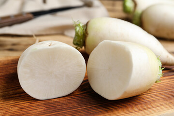 Cut and whole white turnips on wooden board, closeup