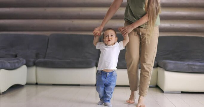 Baby boy taking first steps with mother help at home