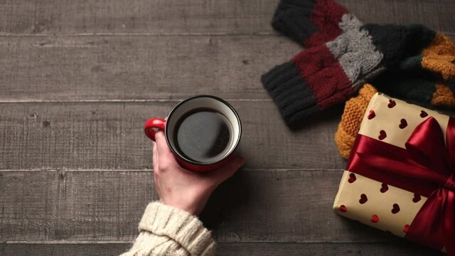 Woman hands with cup of coffee and gift box on wooden table