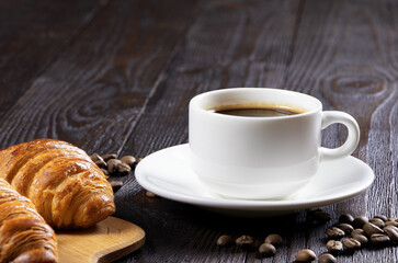 A cup of hot coffee and croissants on a wooden background. Breakfast with coffee and fresh pastry. Copy space. Fresh cake and pastry