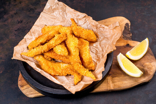 Chicken breaded strips on a black plate with ketchup and french fries.Fried chicken dippers in black bucket with sauce on black background.