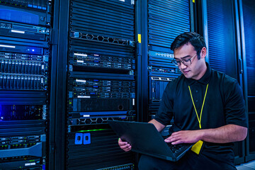 Employee looking at laptop next to server racks