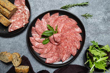 Traditional Italian salami on a black plate served with arugula and multi-grain baguette