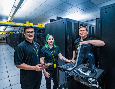 Smiling co-workers with computer in data center server room