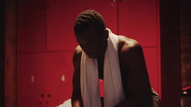 Dark-skinned young man sits in a locker room with a towel around his neck