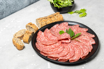 Traditional Italian salami on a black plate served with arugula and multi-grain baguette