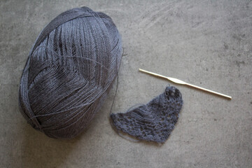 Ball of grey wool yarn, crochet hook on grey background with copy space. Crochet pattern close up...