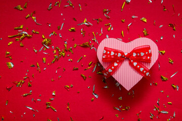 heart shaped gift box on red background with festive glitter particles