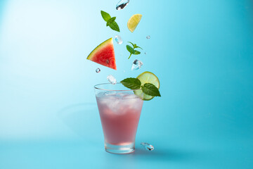 Watermelon cocktail with ice cubes,mint lives and lime on blue background.Shot of drink in freeze motion,flying ice,mint leaves and watermelon.Drink levitation.