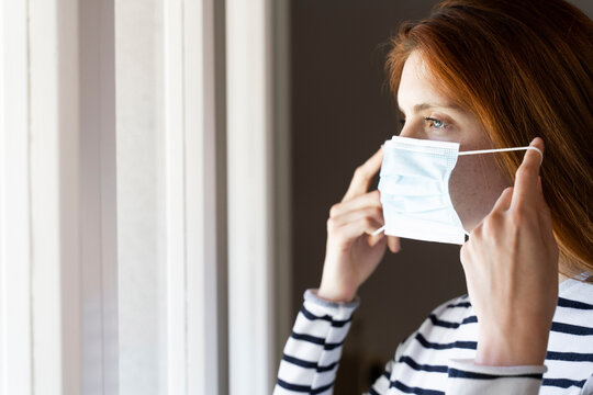 Young woman wearing protective face mask while standing at home during COVID-19