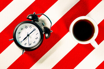 Mug of coffee and alarm clock on white and red striped pattern