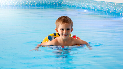 Fototapeta na wymiar Happy smiling little boy swimming in indoor swimming pool.