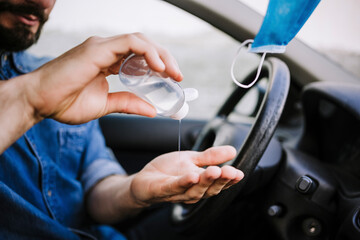 Young man using hand sanitizer in car during COVID-19