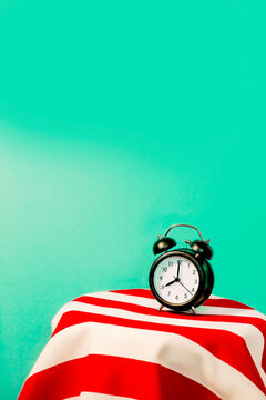Studio shot of alarm clock standing on white and red striped pattern