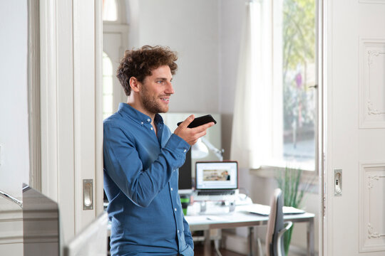 Male professional sending voicemail through mobile phone at office