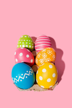 Variation of design and hand colored Easter eggs in tray on pink background