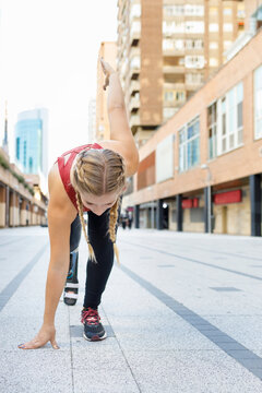 Athlete with prosthetic leg crouching for sports race on footpath