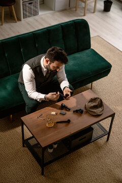 Bearded man sitting on sofa preparing smoking pipe