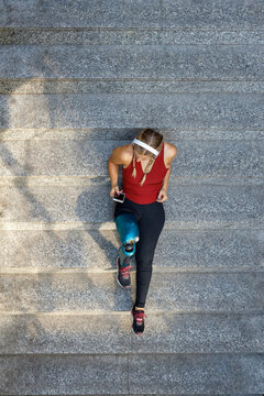 Young amputee wearing headphones using mobile phone while sitting on steps