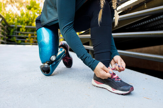 Athlete with prosthetic leg tying shoe lace while kneeling on bridge